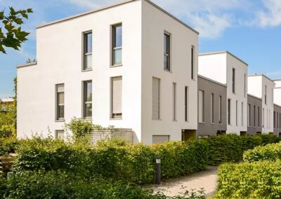 Galerie-Motiv Wohnbau: Reihenhaus / Doppelhaushälfte. Bild mehrerer moderner Reihehäuser in warmen Beige- und Brauntönen sowie üppiger Begrünung