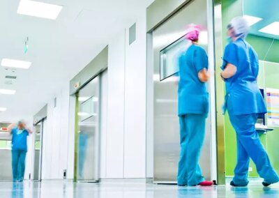 Galerie-Motiv Zweckbau: Krankenhaus. Bild eines hellen, modernen Krankhausflurs mit Personal in blauer OP-Kleidung